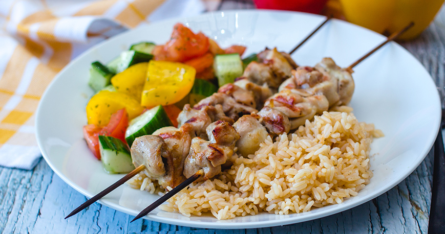 chicken souvlaki skewers on a plate with rice and vegetables