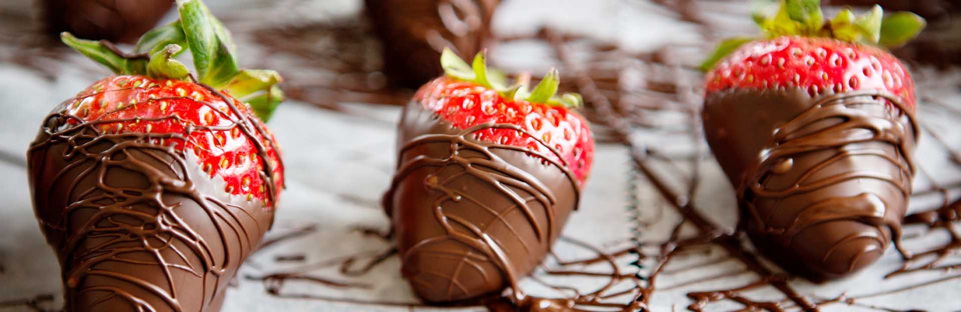 Three chocolate covered strawberries sitting on parchment paper.