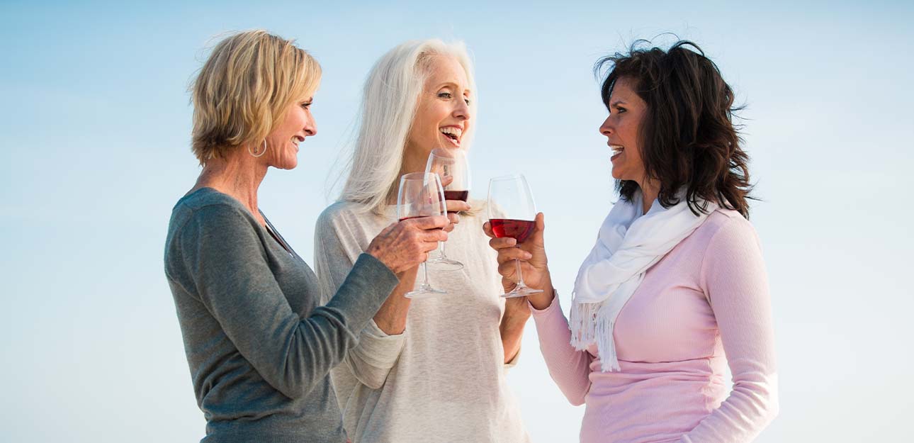 Three ladies standing together drinking wine.